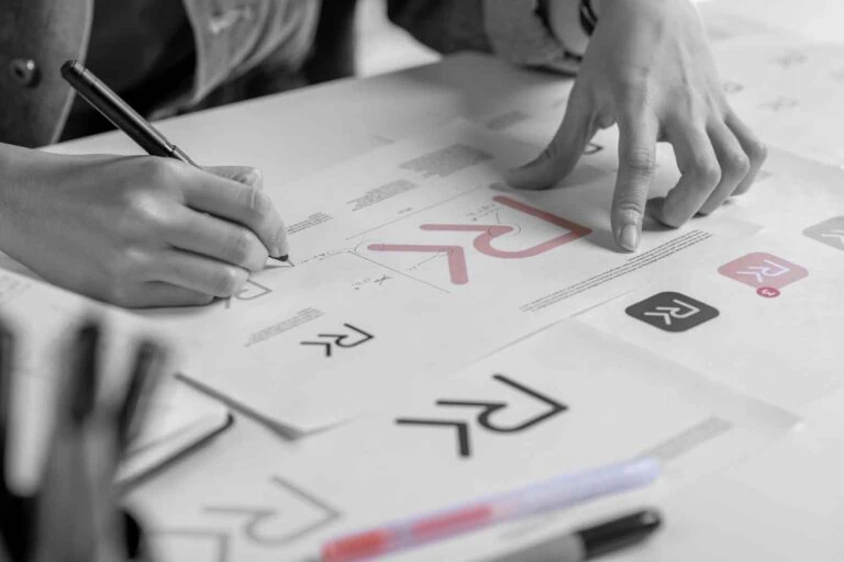 Designer macht Notizen zu Logo-Entwürfe auf ausgebreiteten Papierbögen für spätere Abstimmungsprozesse
